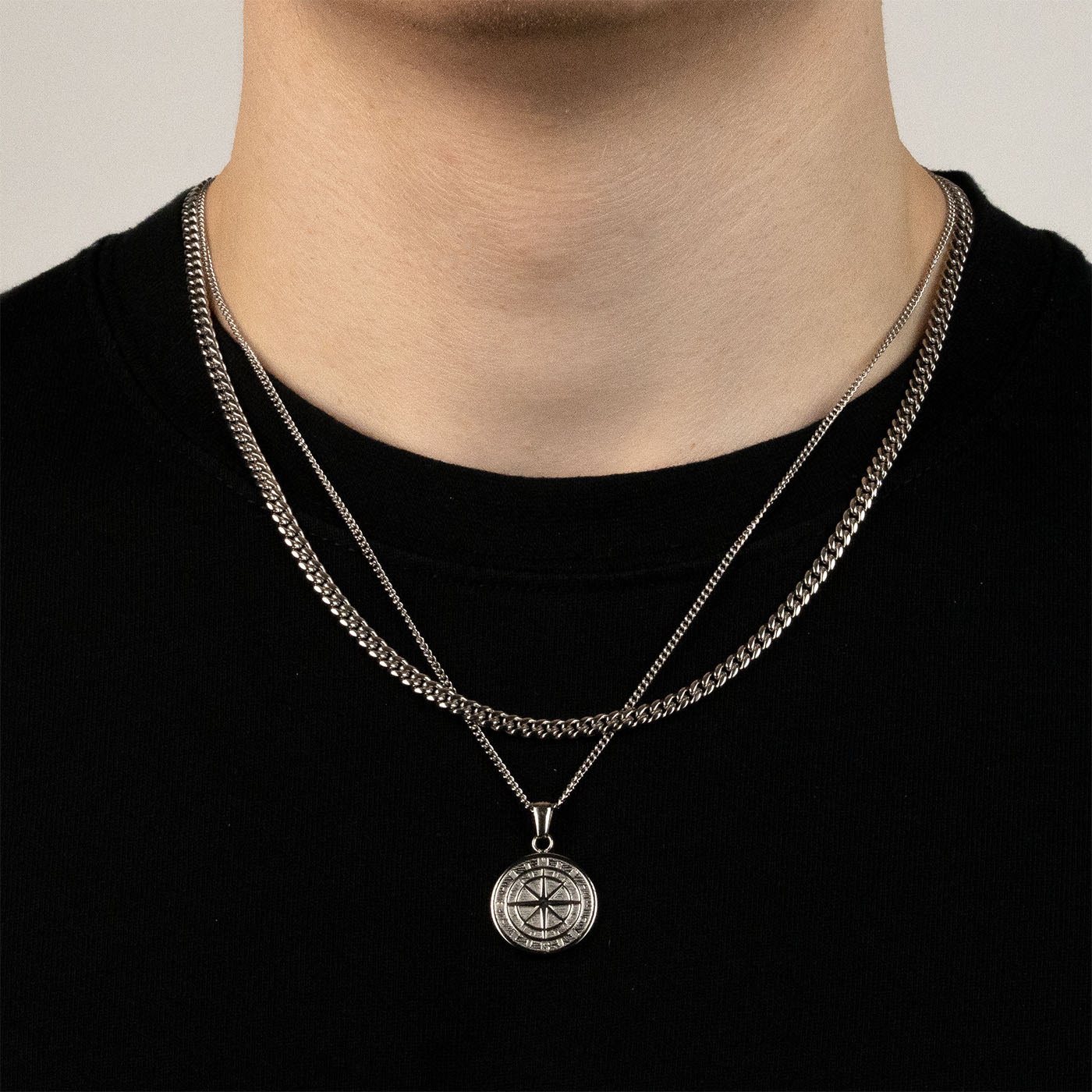 Model trägt ein silberfarbenes Schmuckset aus einer Cuban-Halskette und einem Kompass-Anhänger aus 316L Edelstahl mit einem Gesamtgewicht von 20,7 g.