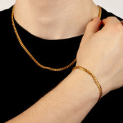 Model trägt ein goldfarbenes Schmuckset aus einer Cuban-Halskette und einem passenden Cuban-Armband aus 316L Edelstahl mit einem Gesamtgewicht von 23,0 g.
