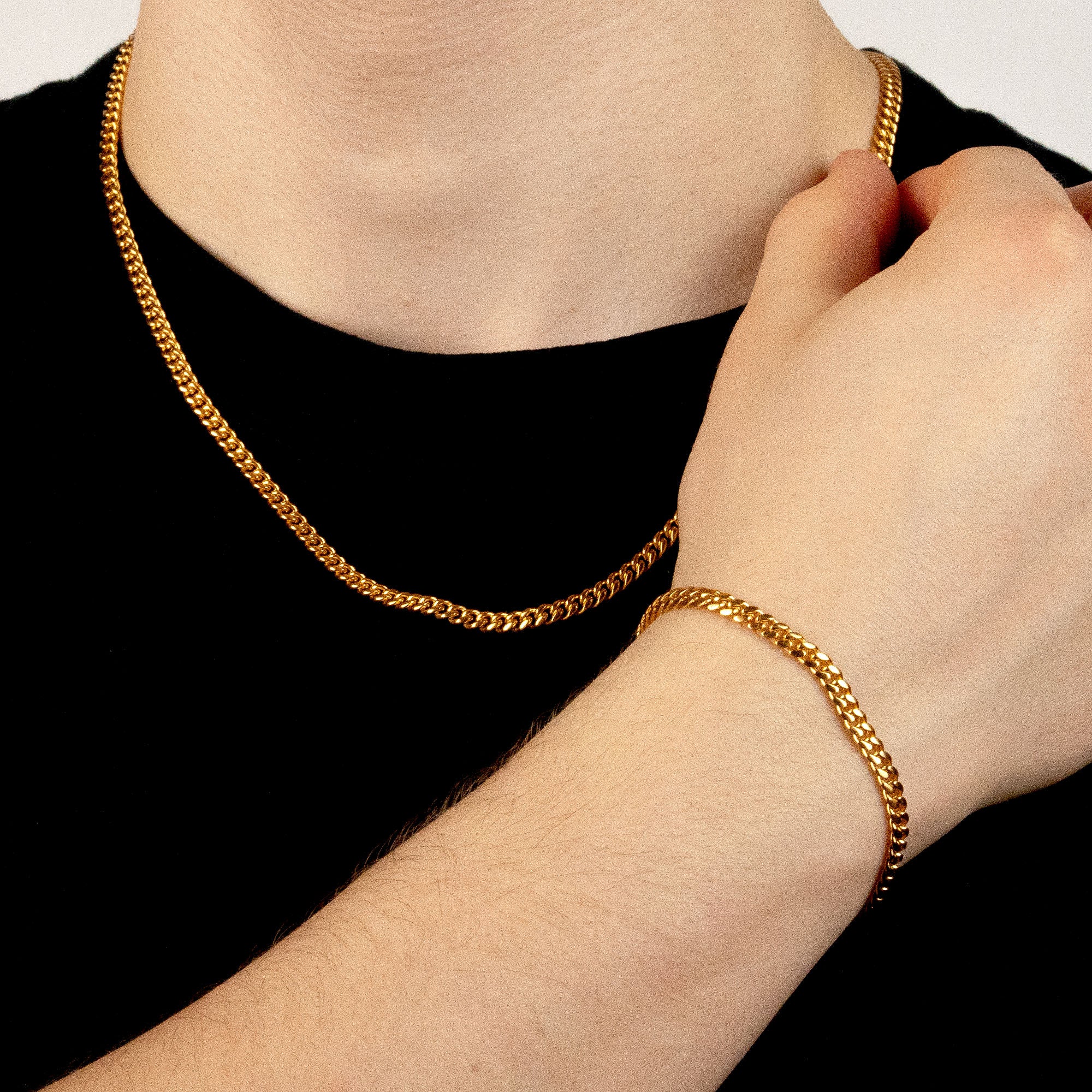 Model trägt ein goldfarbenes Schmuckset aus einer Cuban-Halskette und einem passenden Cuban-Armband aus 316L Edelstahl mit einem Gesamtgewicht von 23,0 g.